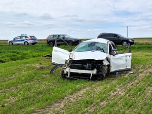 Uszkodzony pojazd koloru białego stoi na trawie. W tle widać radiowóz policyjny.
