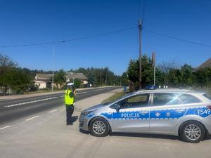 radiowóz policyjny, obok funkcjonariusz Policji dokonujący pomiaru prędkości.