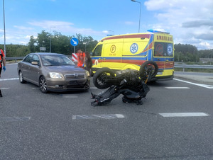 Miejsce zdarzenia drogowego. Na drodze stoi samochód osobowy marki Toyota, wywrócony motocykl oraz karetka pogotowia.