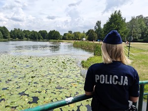 Policjantka kontroluje stan bezpieczeństwa na kąpielisku miejskim. W tle widać wyznaczoną strefę do kąpania.