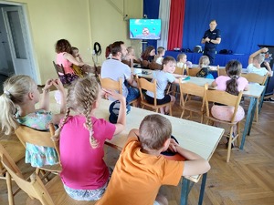 Policjant opowiada dzieciom o bezpieczeństwie nad wodą. Dzieci siedzą przed policjantem.