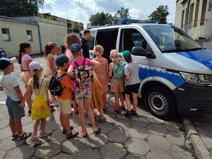 Policjant omawia budowę policyjnego radiowozu. Dzieci stoją przed policjantem.