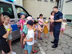 Policjant rozdaje stojącym przed nim dzieciom odblaski.