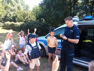 Policjant omawia zasadę działania kajdanek. Dzieci są przebrane za policyjny patrol.