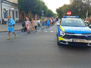 Pielgrzymi maszerują ulicami Łasku. Na jezdni stoi policyjny radiowóz.