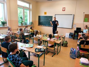 Policjant opowiada pierwszoklasistą o bezpieczeństwie w drodze do szkoły.