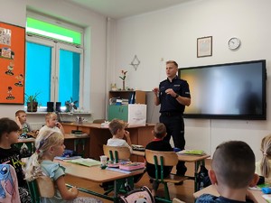 Policjant opowiada pierwszoklasistą o bezpieczeństwie w drodze do szkoły.