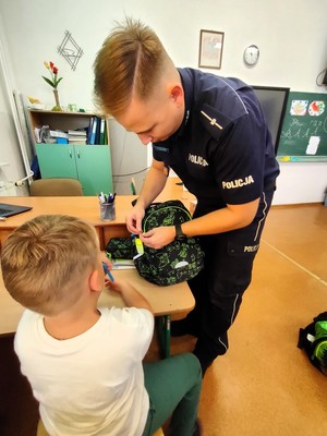 Policjant przyczepia chłopcu do plecaka odblask.