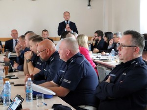 Policjanci siedzą przy stole. W tle widać przemawiającego Wójta Gminy Sędziejowcie.