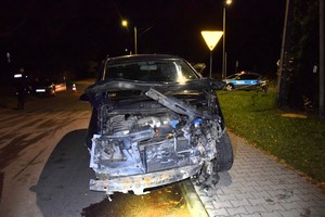 Uszkodzony samochód marki Volkswagen. W tle widać policyjny radiowóz i pracujących policjantów.