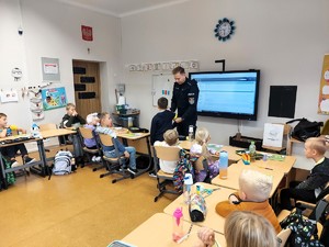 Policjant zakłada chłopczykowi opaskę odblaskową na ramie.