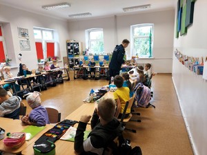 Policjant rozdaje dzieciom siedzącym w ławkach odblaski.