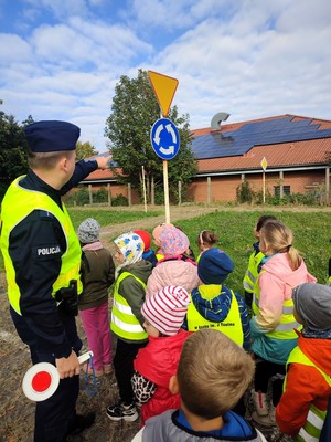 Policjant wskazuje ręką znak &quot;skrzyżowanie o ruchu okrężnym&quot;.