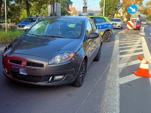 Uszkodzony pojazd marki Fiat. W tle widać policyjne radiowozy oraz przejście dla pieszych.