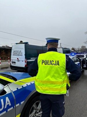 Policjant w kamizelce odblaskowej stoi przed pojazdami policji.