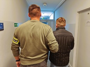 Nieumundurowany policjant trzyma pod rękę zatrzymanego mężczyznę.