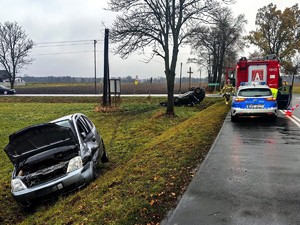 Miejsce zdarzenia drogowego. Samochód marki opel stoi uszkodzony w rowie. W tle widać czarny samochód który stoi na dachu.