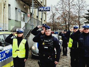 Policjanci oddają honor, stoją przed policyjnymi radiowozami.