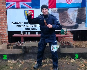 Policjant cieszy się, na szyi ma medal za ukończenie maratonu komandosa.