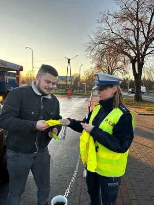 Policjantka wręcza mężczyźnie odblaski i worek odblaskowy.