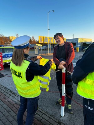 Policjantka wręcza mężczyźnie kamizelkę odblaskową. Mężczyzna się uśmiecha.