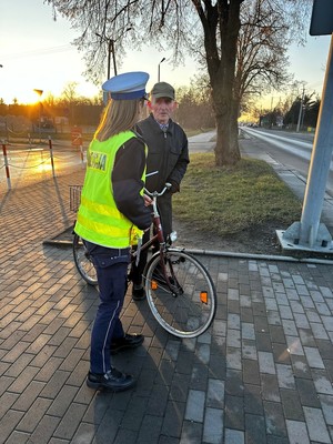 Policjantka rozmawia z rowerzystą o bezpieczeństwie na drodze i wręcza mu odblask.