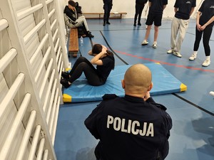 Policjant mierzy czas. Uczennica wykonuje brzuszki leżąc na materacu.