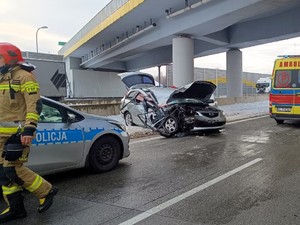 Miejsce zdarzenia drogowego. Na drodze stoi uszkodzony pojazd oraz policyjny radiowóz i karetka pogotowia.