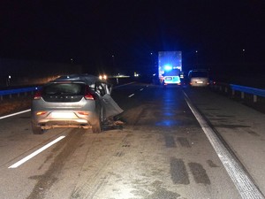 Miejsce zdarzenia drogowego. Na środku drogi stoi uszkodzony pojazd marki Volvo. W tle widać pojazd ciężarowy oraz policyjny radiowóz.