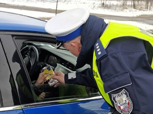 Policjant wręcza zawieszkę zapachową z napisem zwolnij.