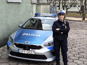 Przed radiowozem policyjnym stoi policjantka.