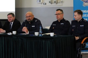 Przy stole siedzą policjanci. Jeden przemawia do mikrofonu.