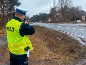 Policjant stoi przy drodze i mierzy prędkość pojazdów.