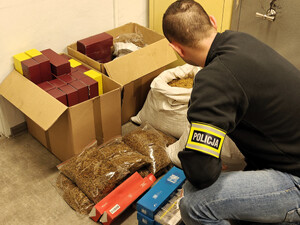 Policjant kuca przy zatrzymanym tytoniu. Liczy nielegalne papierosy.