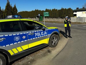 Policjantka mierzy prędkość pojazdów. Stoi przy drodze.