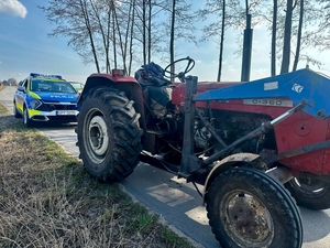 Na drodze stoi ciągnik rolniczy a za nim policyjny radiowóz.