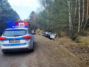 Miejsce zdarzenia drogowego. Na drodze stoi policyjny radiowóz. W tle widać samochod w rowie.