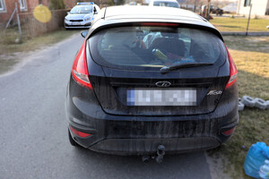 Na drodze stoi czarny ford. Przed nim policyjny radiowóz.