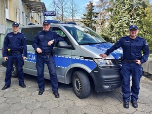 Dzielnicowi stoją przy policyjnym aucie.
