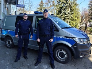 Dwóch policjantów stoi przy policyjnym aucie.