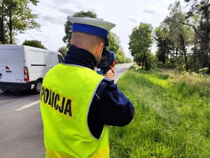 Policjant stoi przy przy drodze i mierzy prędkość.