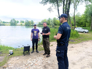 Policjant kontroluje wędkarza łowiącego ryby.