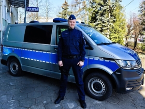 Dzielnicowy stoi przed radiowozem.