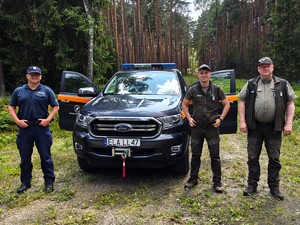 Policjant i starżnicy leśni stoją przy samochodzie.