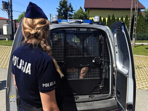 Zatrzymany w policyjnym radiowozie. Przy aucie stoi policjantka.