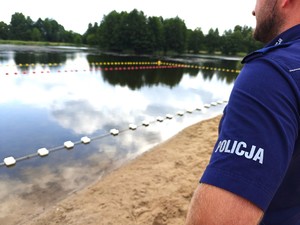 Policjant stoi na plaży i ogląda kąpielisko.