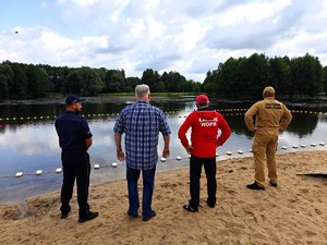 Funkcjonariusze stoją na plaży i oglądają kąpielisko.