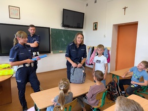 funkcjonariusze policji w mundurach stojący w klasie przy tablicy, w ławkach siedzące dzieci.