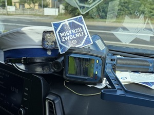 w radiowozie widoczna czapka policyjna, miernik prędkości oraz ulotka &quot;mistrzu Zwolnij&quot;.