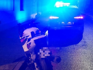 motocykl koloru białego, dalej radiowóz z włączonymi światłami.